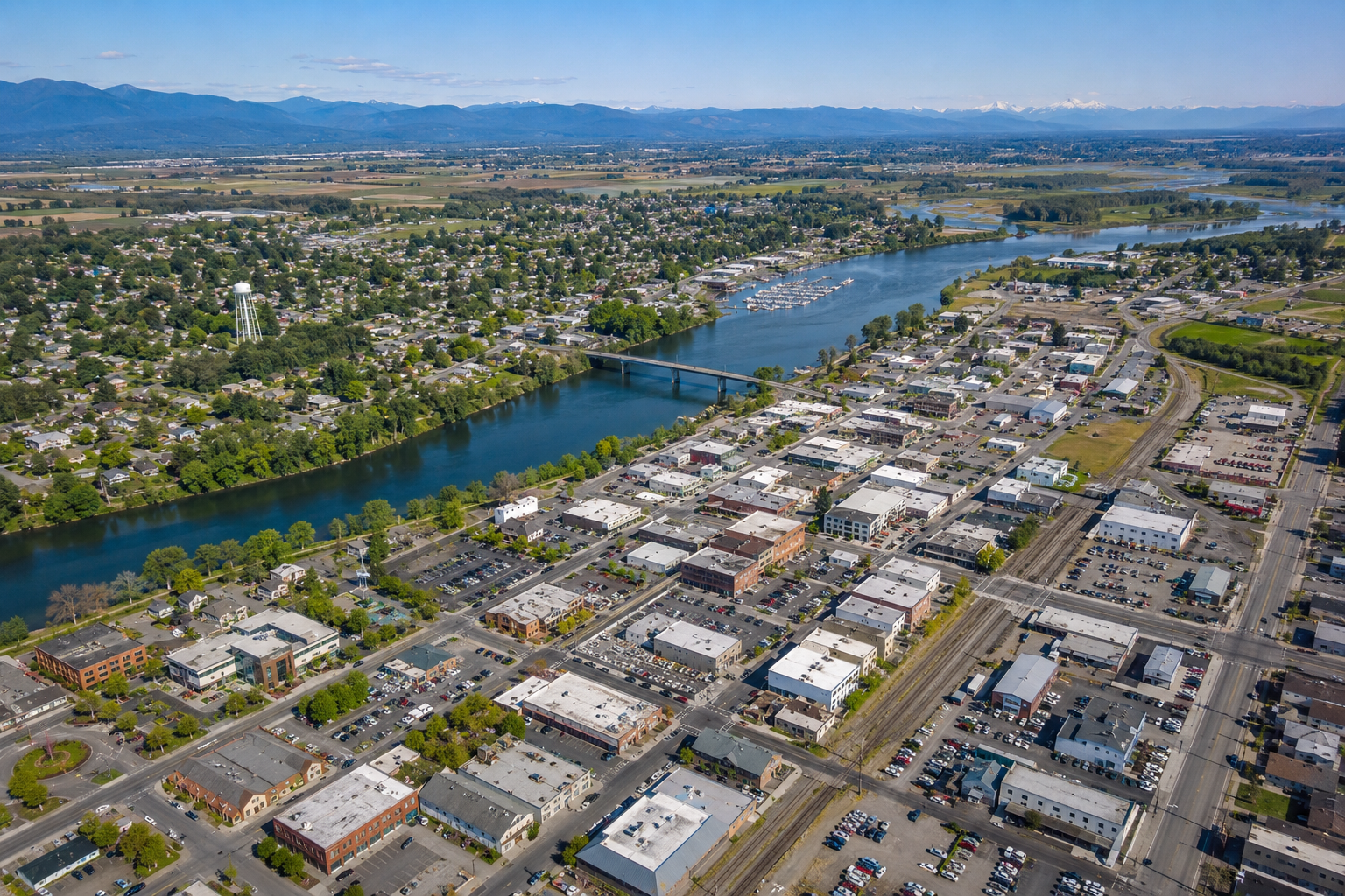 Aerial view of Burlington, WA featuring downtown buildings, the Skagit River, surrounding neighborhoods, and mountain views in Skagit County, Washington